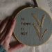 A hand touches an embroidery hoop with Spanish text and flowers beside an open book.